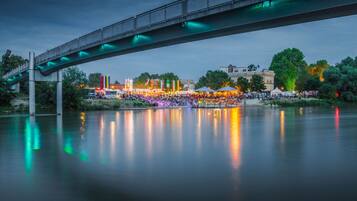A bridge over a calm river reflecting colorful lights, with a crowd and tents in the background.