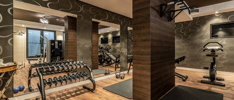 A modern gym with wooden flooring, exercise equipment, and a mirror wall.