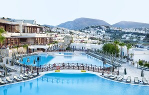 Piscina de un complejo turístico con tumbonas y sombrillas, rodeada de edificios y montañas.