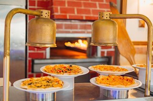 A pizza station with multiple pizzas on white plates, a brick fireplace in the background, and two metal bells above the pizzas.