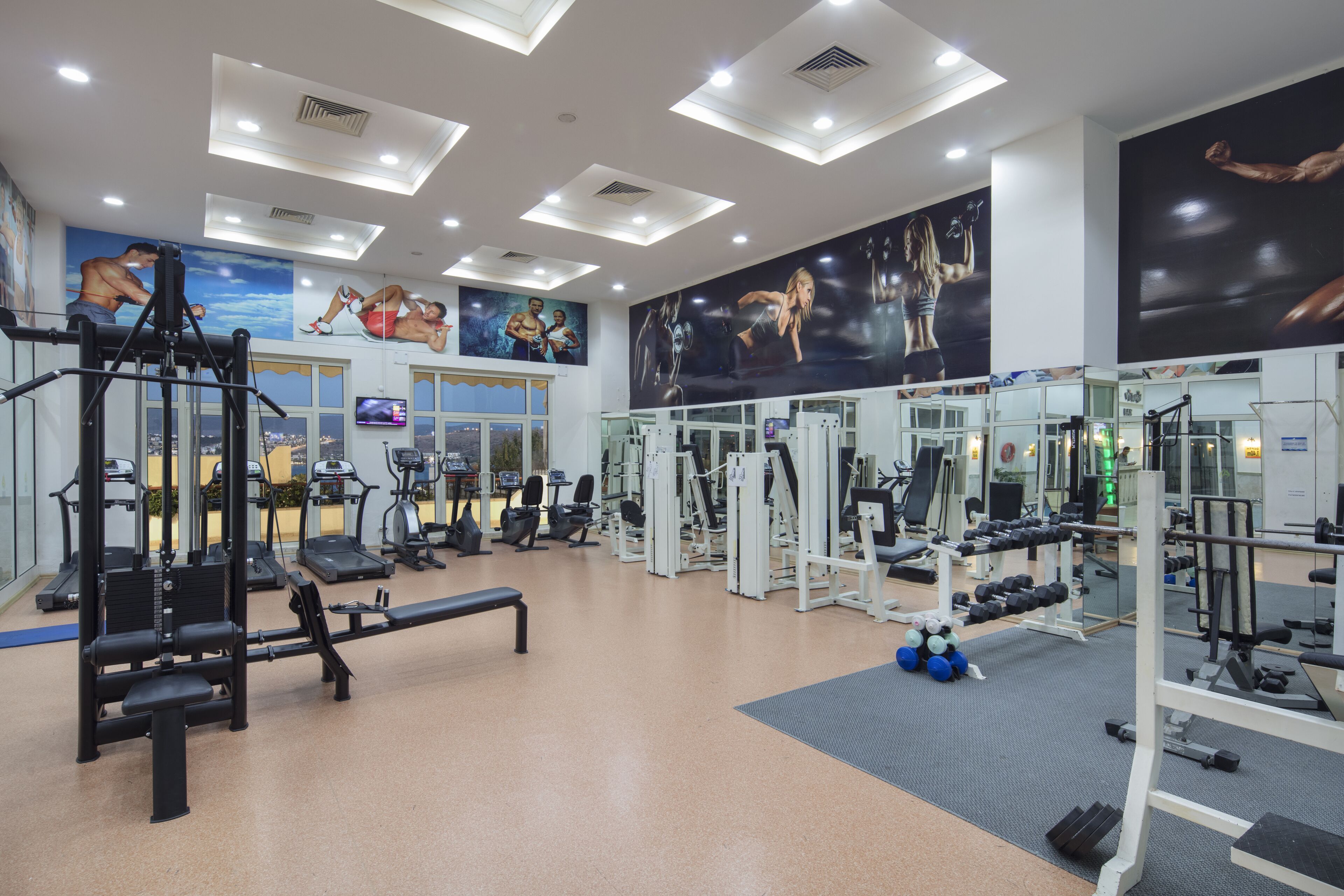 A gym with various exercise equipment, a bench, and a large mural of athletes on the wall.