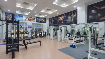 A gym with various exercise equipment, a bench, and a large mural of athletes on the wall.