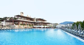 Une piscine avec des chaises longues et des parasols, un bâtiment doté d’un patio couvert et un paysage montagneux en arrière-plan.