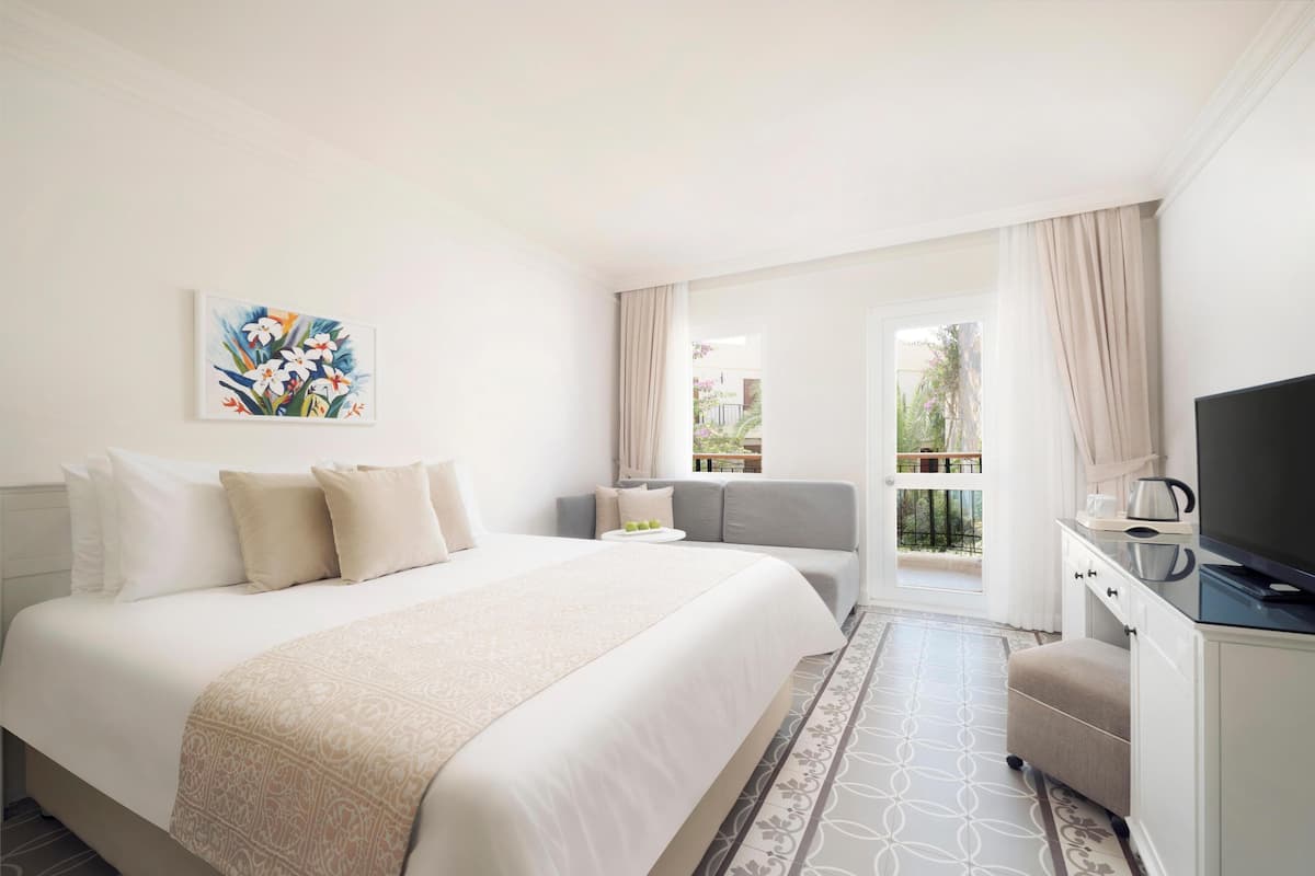 Une chambre d’hôtel avec un grand lit, un canapé, une télévision et un balcon avec des rideaux.