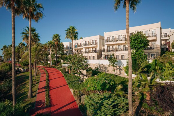 Un hôtel à plusieurs étages, avec un chemin rouge et des palmiers.