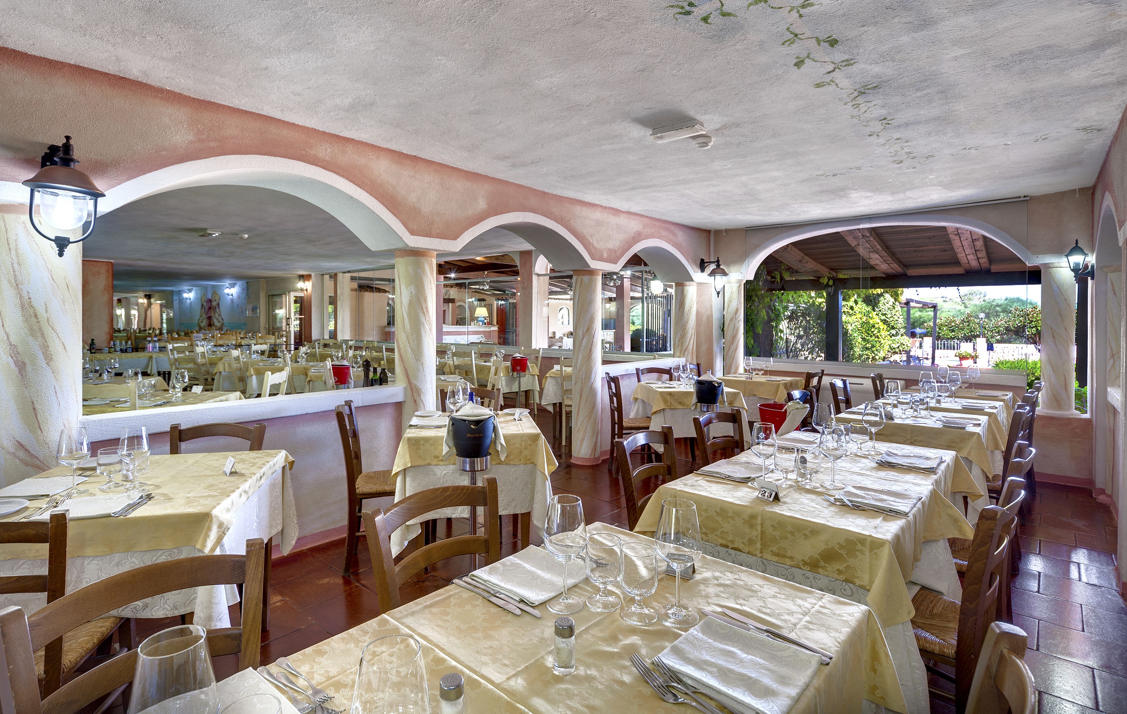 Un restaurant doté de nombreuses tables dressées pour le service, avec un décor intérieur classique caractérisé par des arches et un sol carrelé.
