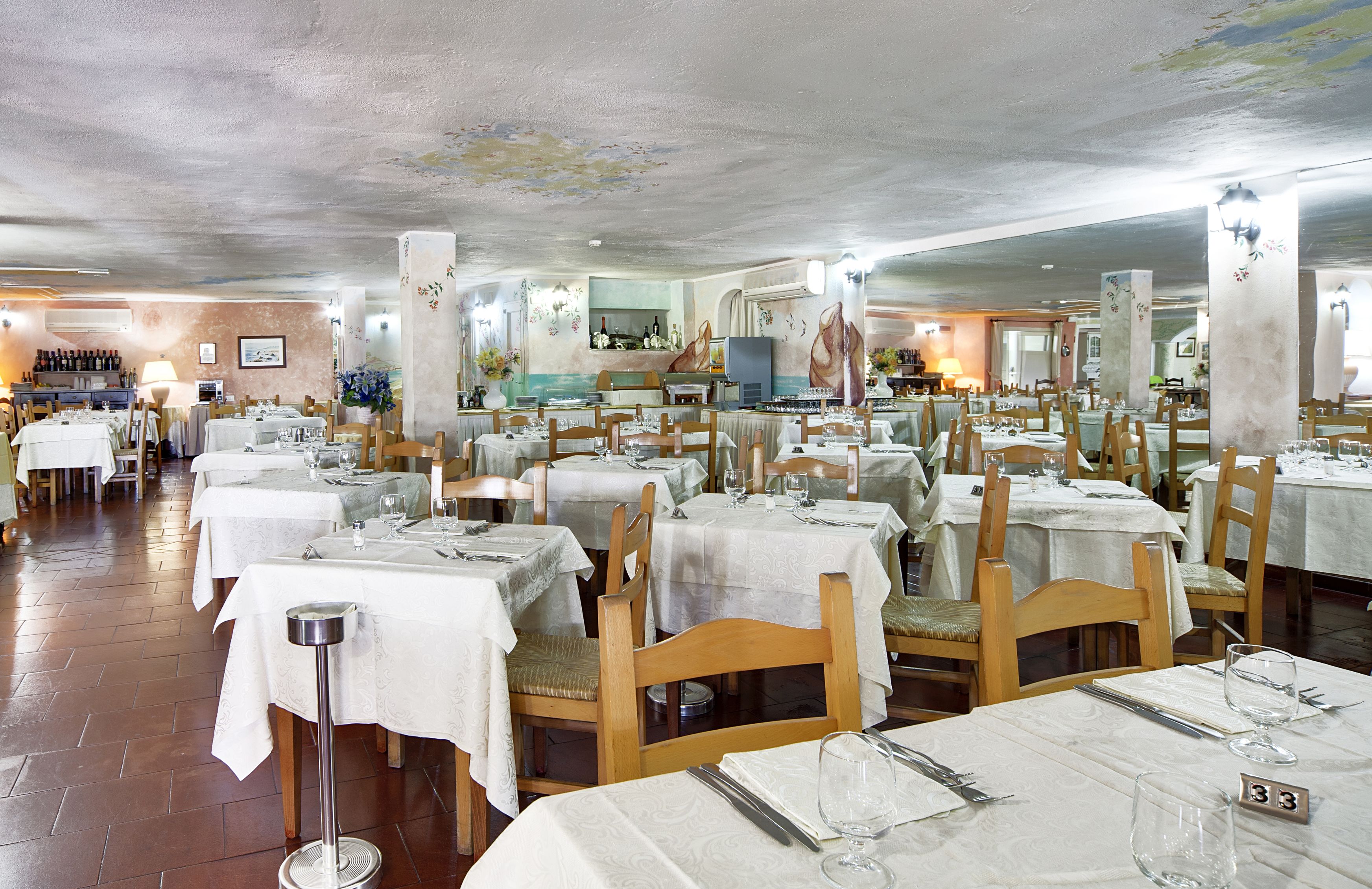 A restaurant with multiple tables set for dining, wooden chairs, and a tiled floor.