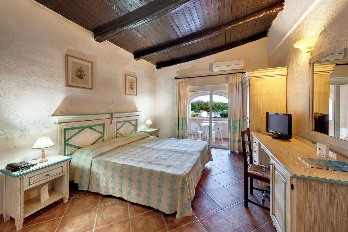 A bedroom with a bed, bedside table, lamp, and a TV.