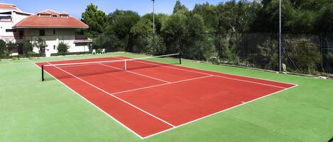 A tennis court with a net, surrounded by a fence and trees.