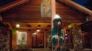 A wooden cabin with a stone foundation, a bear statue, and a lit sign. - Robinhood Resort (Big Bear Lake)