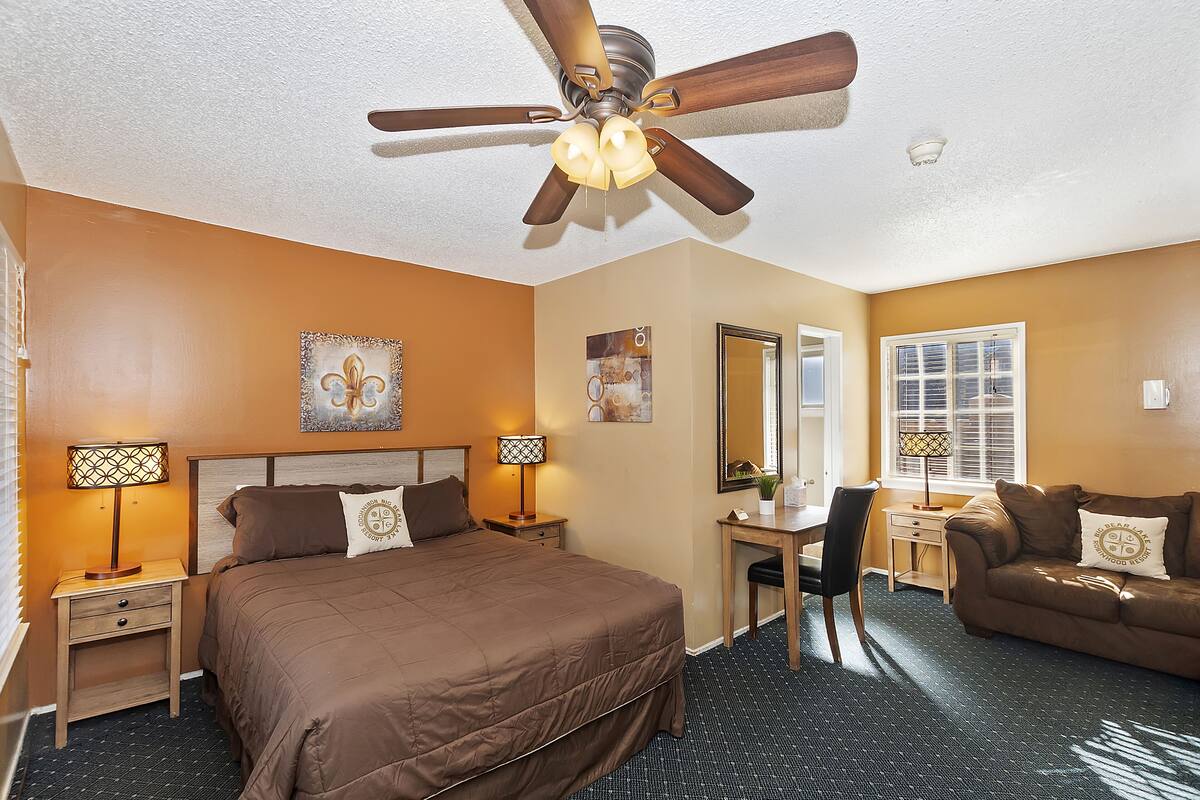 Une chambre d’hôtel avec un grand lit, un bureau, une chaise, un canapé, un ventilateur de plafond et une fenêtre.