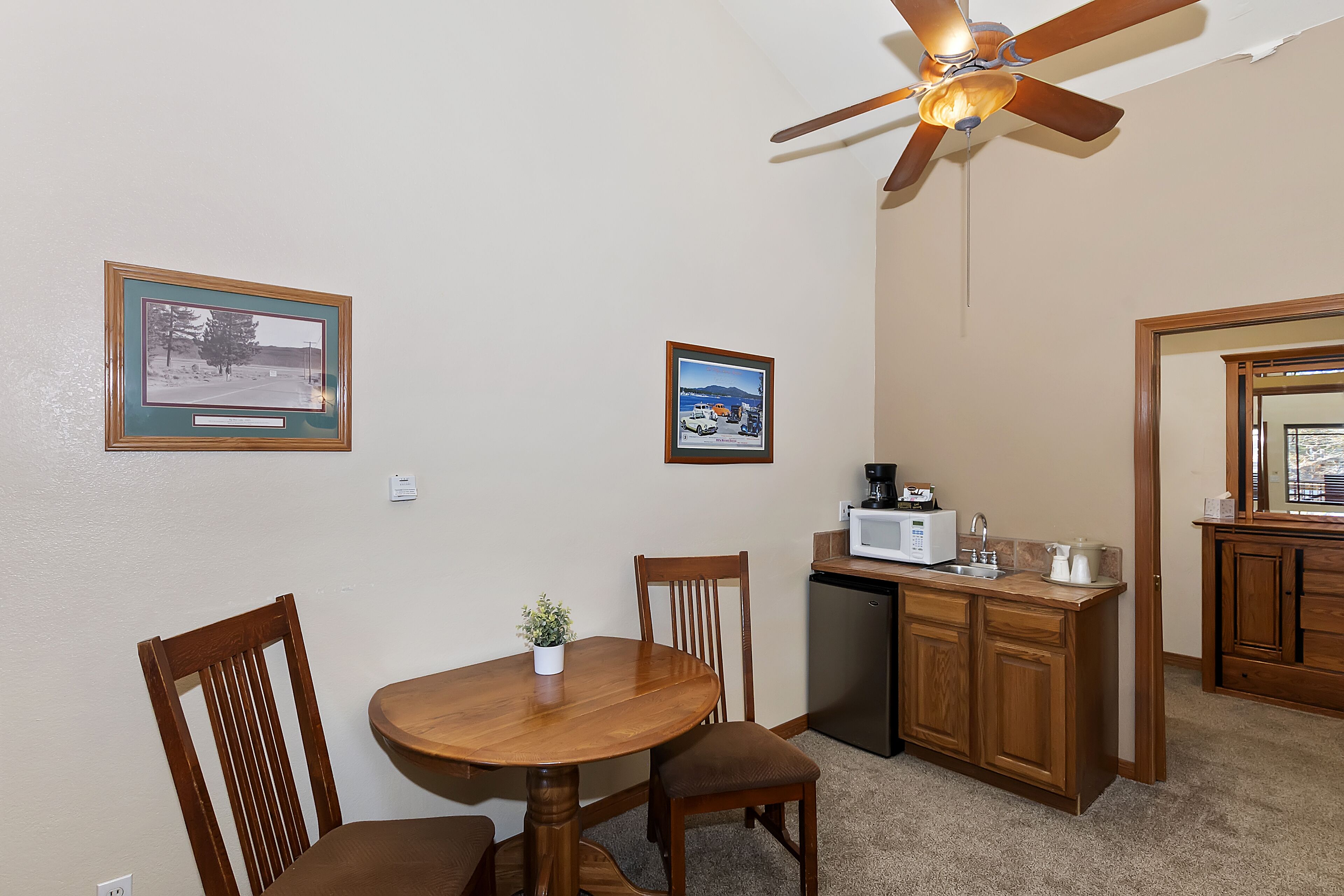 A compact kitchen with a dining area, wooden cabinets, a ceiling fan, and two framed pictures on the wall.