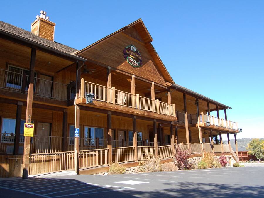 A wooden lodge with a balcony, a sign indicating a restaurant, and a parking lot.