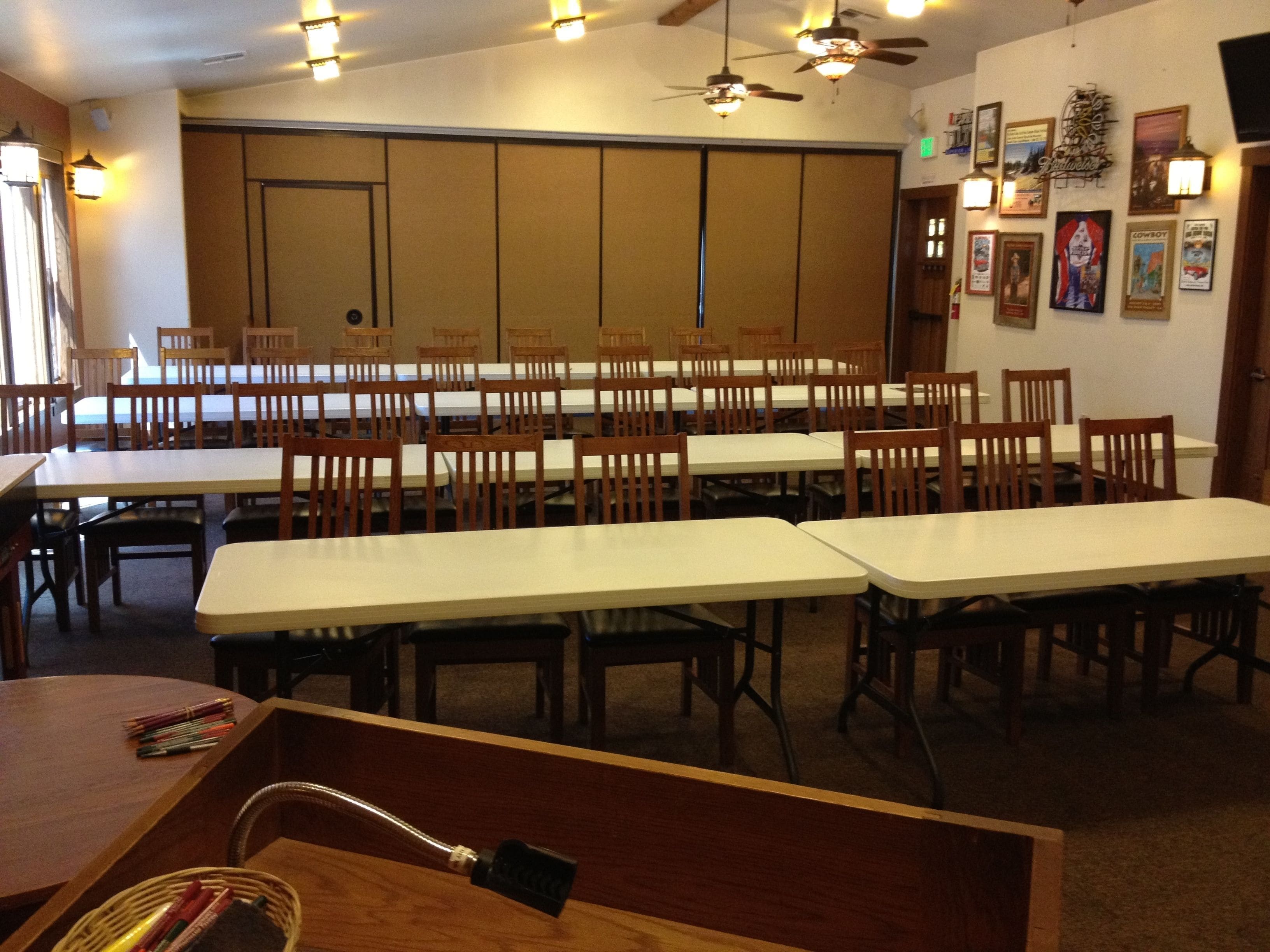 A conference room with multiple tables and chairs, ceiling fans, and wall-mounted lights.