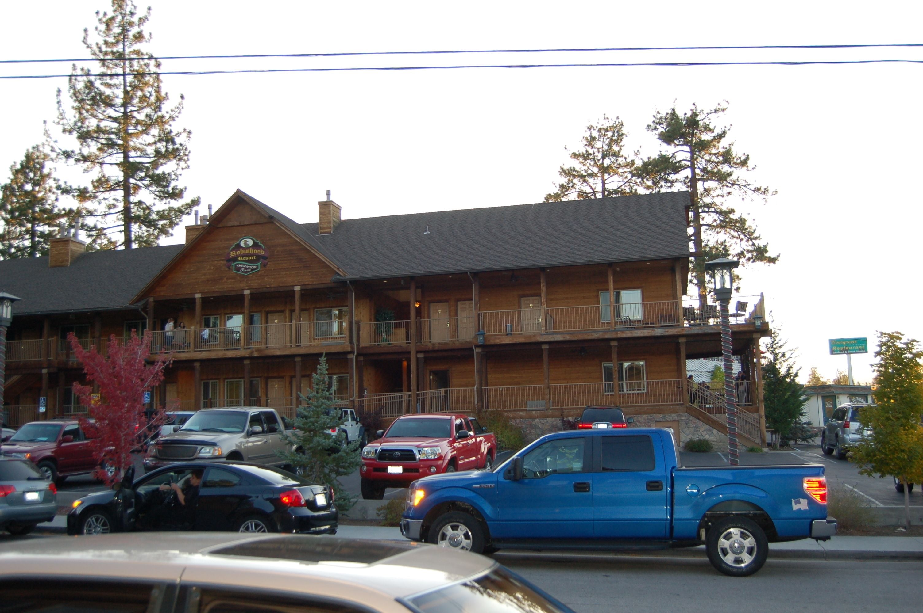 A multi-story wooden building with balconies, a parking lot, and a visible sign indicating a business establishment.