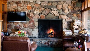 A stone fireplace with a TV mounted above it, leather sofas, and a wooden ceiling fan in a cozy living room. - Robinhood Resort (Big Bear Lake)