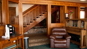 A wooden interior with a staircase, a leather chair, a fireplace, and a coffee station. - Robinhood Resort (Big Bear Lake)