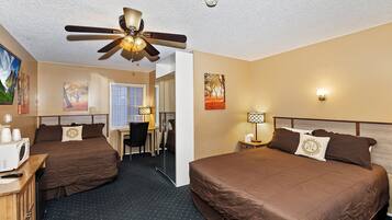 A hotel room with two beds, a desk, a chair, a ceiling fan, and artwork on the walls.