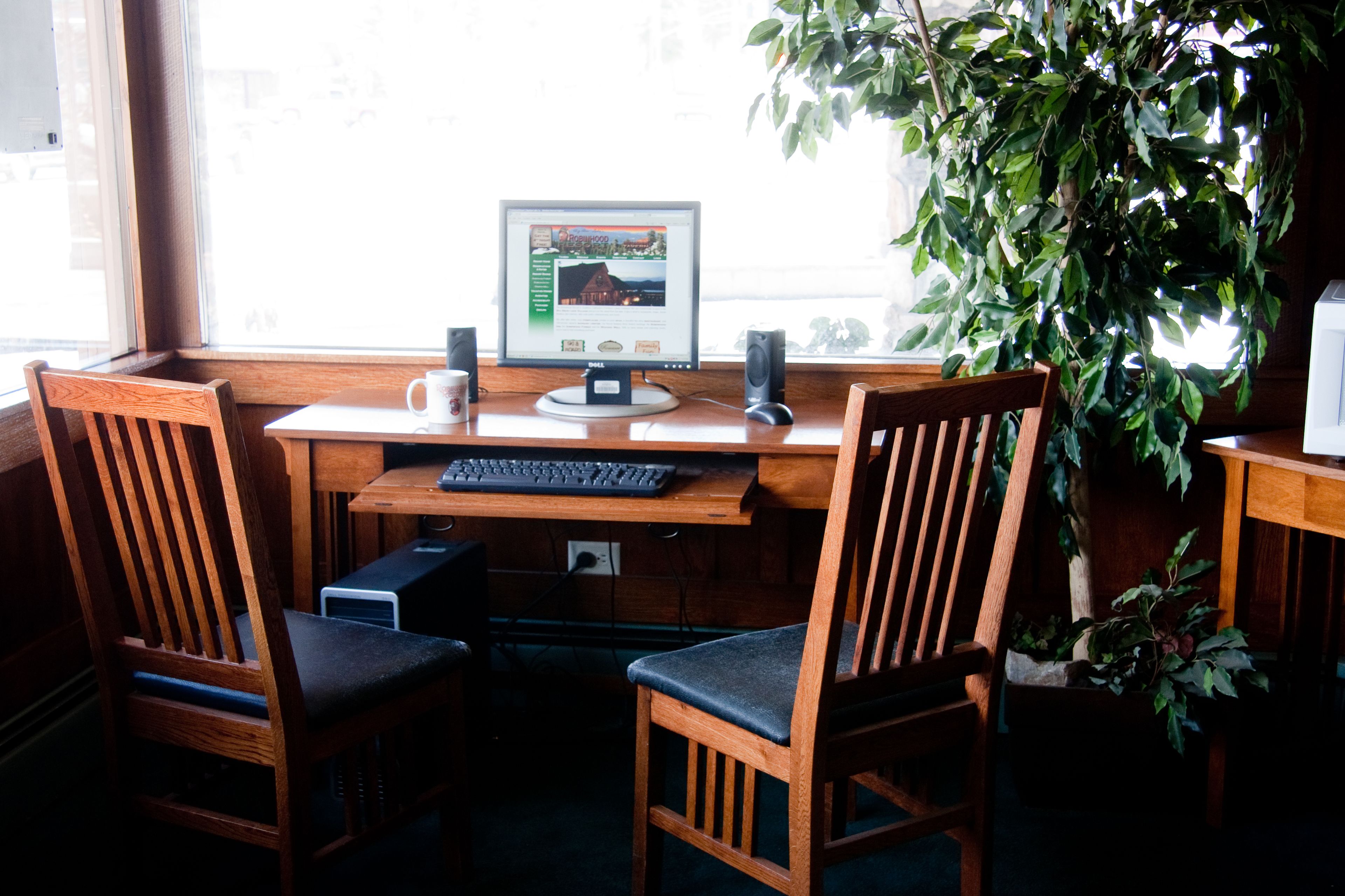 A wooden desk with a computer, two chairs, and a potted plant.