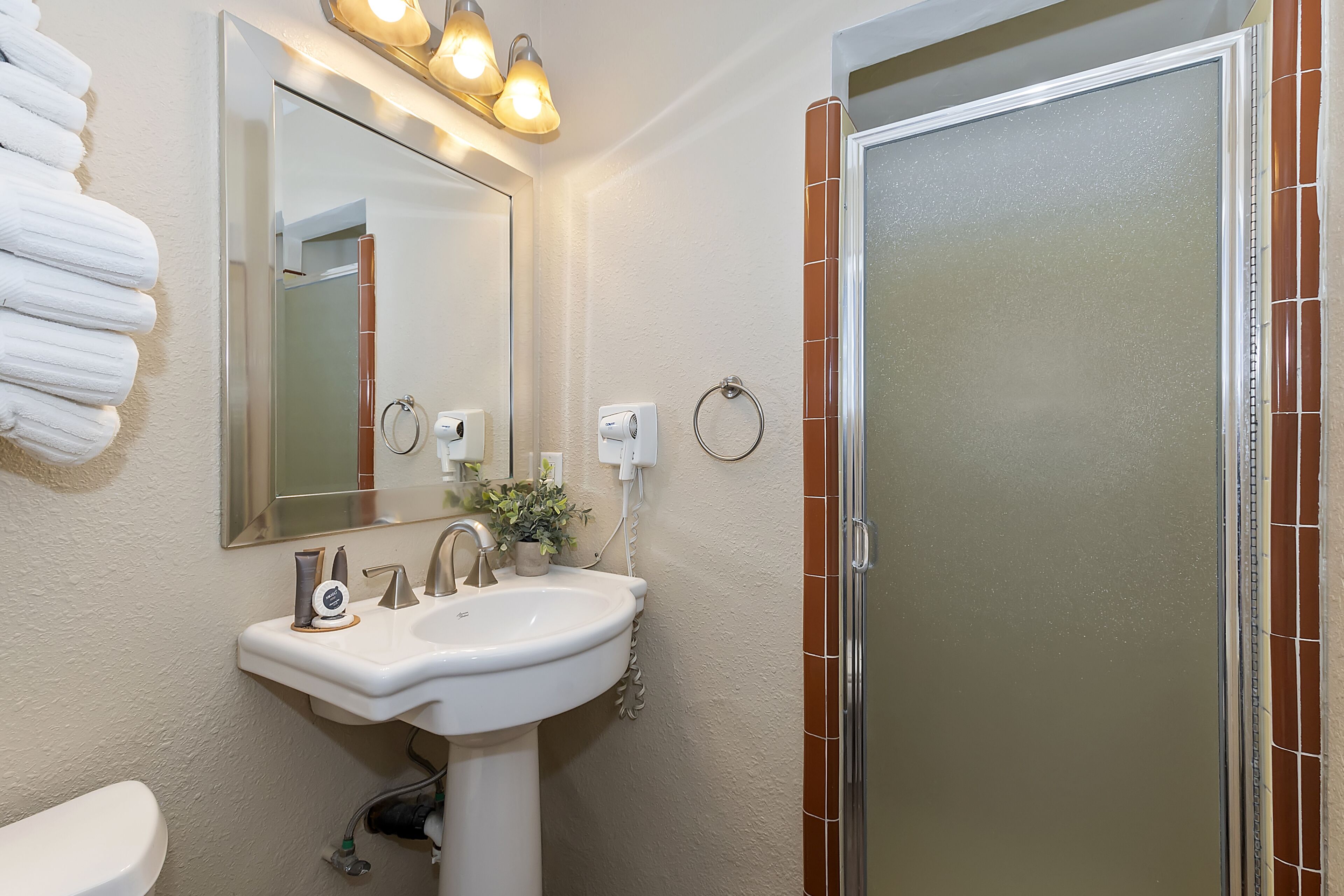 Un baño con lavamanos blanco, un espejo y una ducha con azulejos marrones.