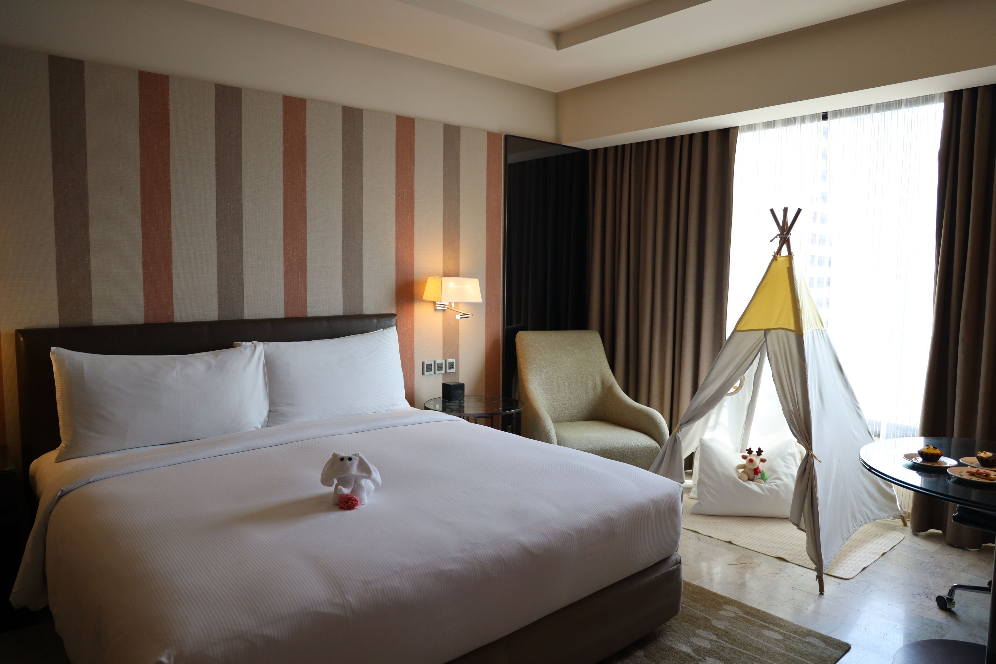 Habitación de hotel con una cama grande, una silla, una mesita, una lámpara y una tienda tipi.