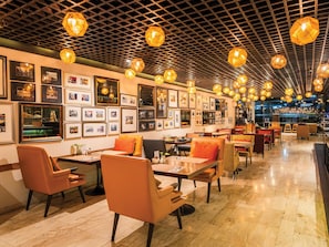 A restaurant with a grid-patterned ceiling, framed pictures on the walls, and a variety of seating arrangements.