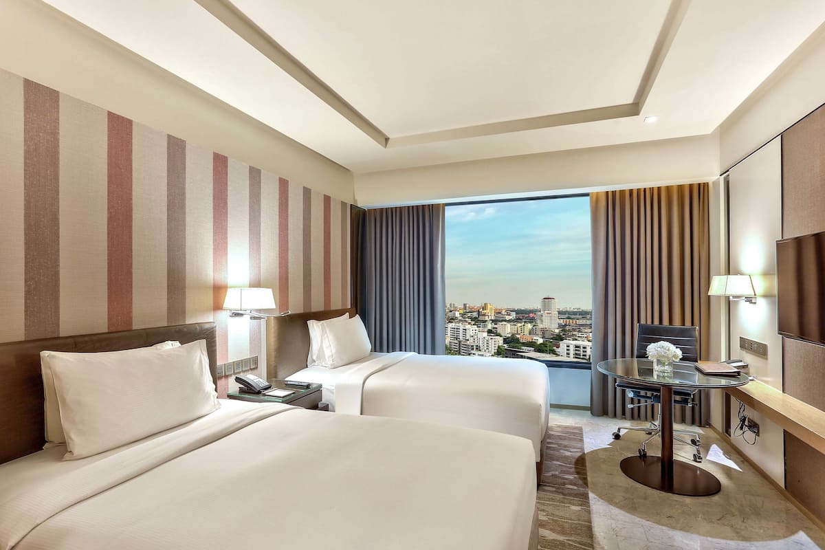 A hotel room with two beds, a desk, and a view of the city.