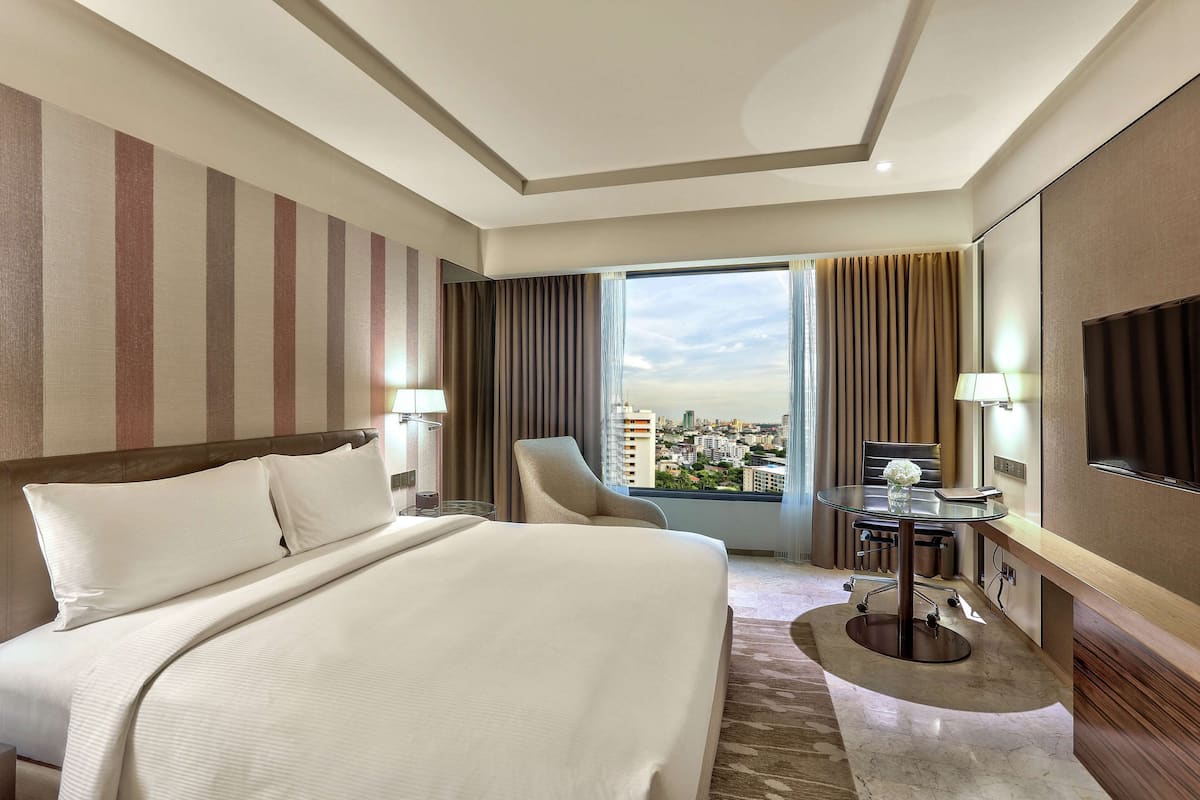 A hotel room with a large bed, a desk, a chair, a TV, and a view of the city.