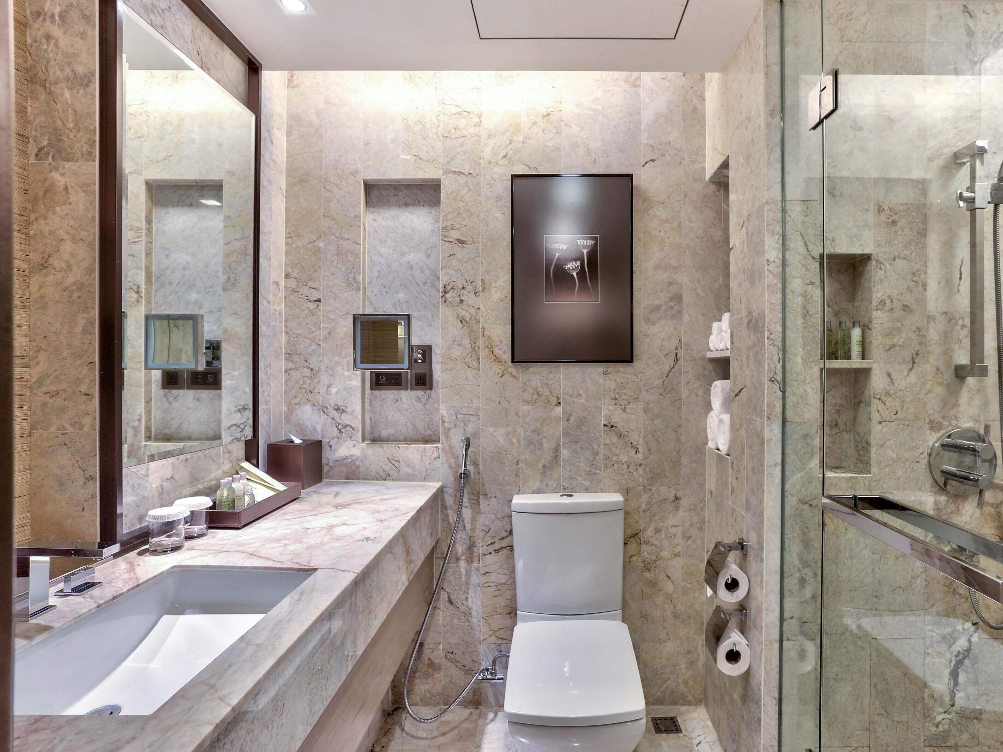 A modern bathroom with a large mirror, two sinks, a toilet, and a glass-enclosed shower area.