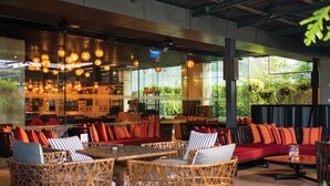 A modern restaurant with wicker furniture, hanging lights, and a view of greenery outside. - DoubleTree by Hilton Sukhumvit Bangkok (Bangkok)