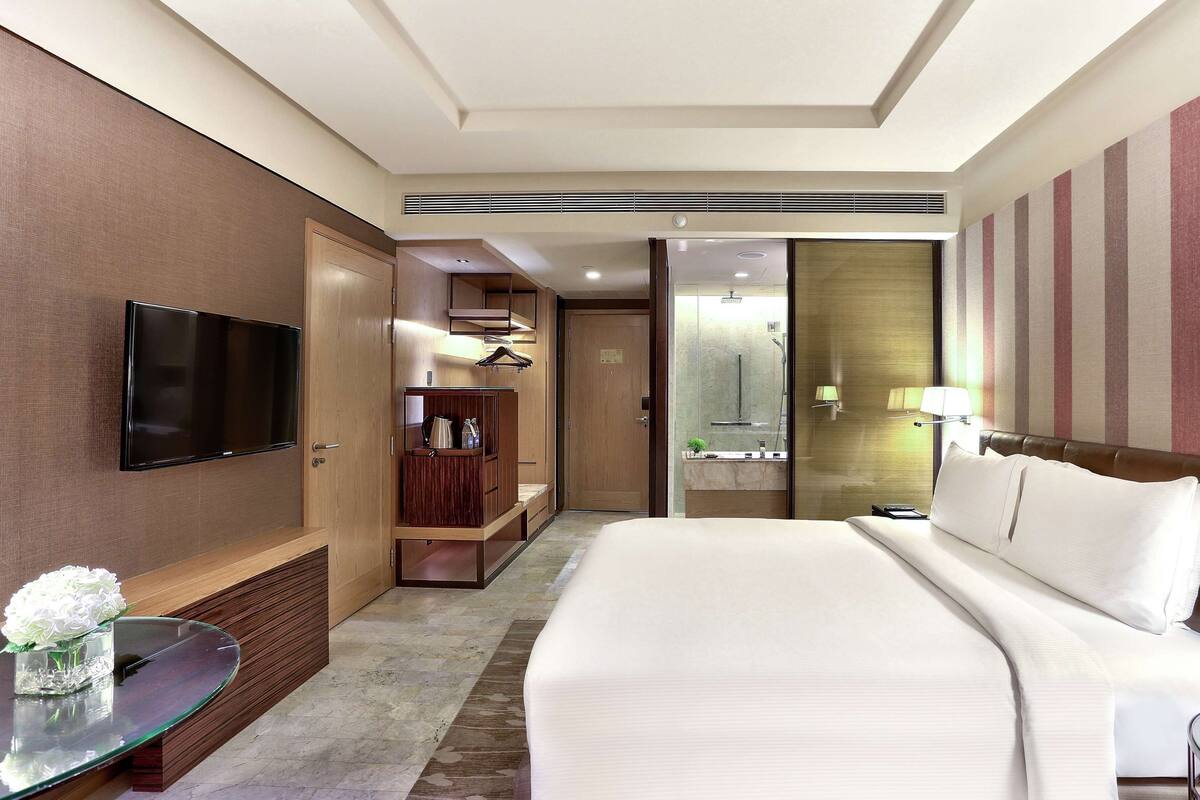 A hotel room with a bed, a TV, a wardrobe, a bathroom, and a small table with a vase of flowers.