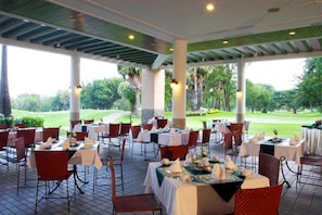 An outdoor dining area with tables and chairs, surrounded by greenery and a golf course view. - Lake View Resort & Golf Club (Cha-am)
