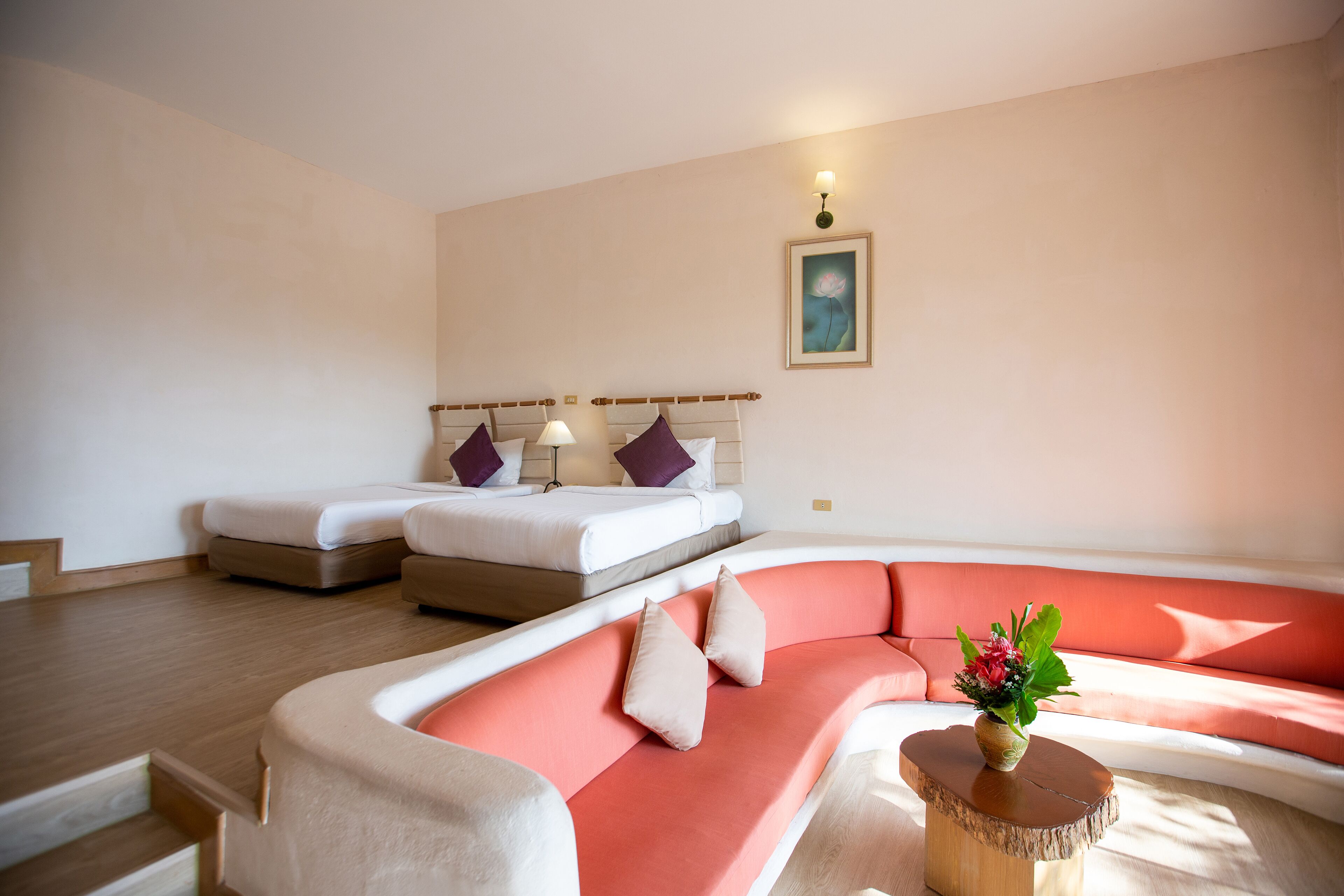 Une chambre d’hôtel moderne avec un canapé incurvé, un lit doté d’une tête de lit en bois et une petite table sur laquelle est posé un vase de fleurs.