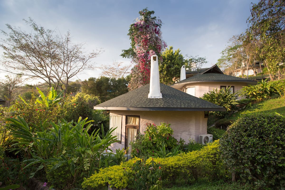 A house with a sloped roof, surrounded by lush greenery and flowering plants.