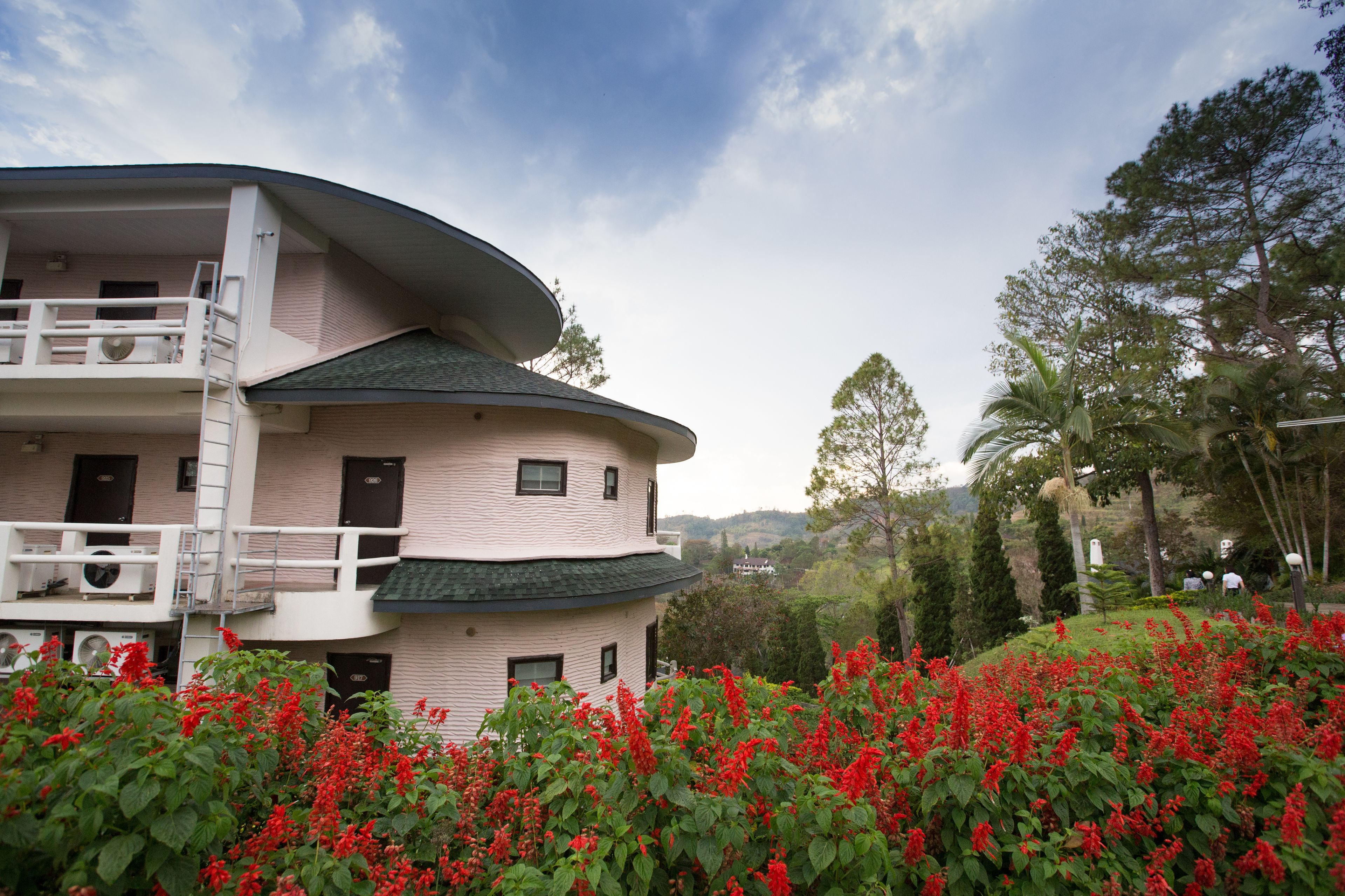 Un immeuble à plusieurs étages, doté de balcons et d’un jardin où l’on peut admirer des fleurs rouges.