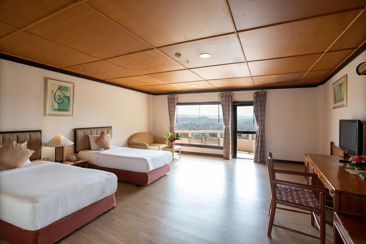 A hotel room with two beds, a desk with a TV, and a balcony with a view.