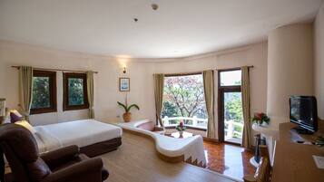 A hotel room with a bed, a sofa, a TV, and a balcony with a view of trees.