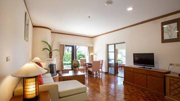 A spacious living room with a wooden floor, a sofa, a TV, and a dining area with chairs and a table.