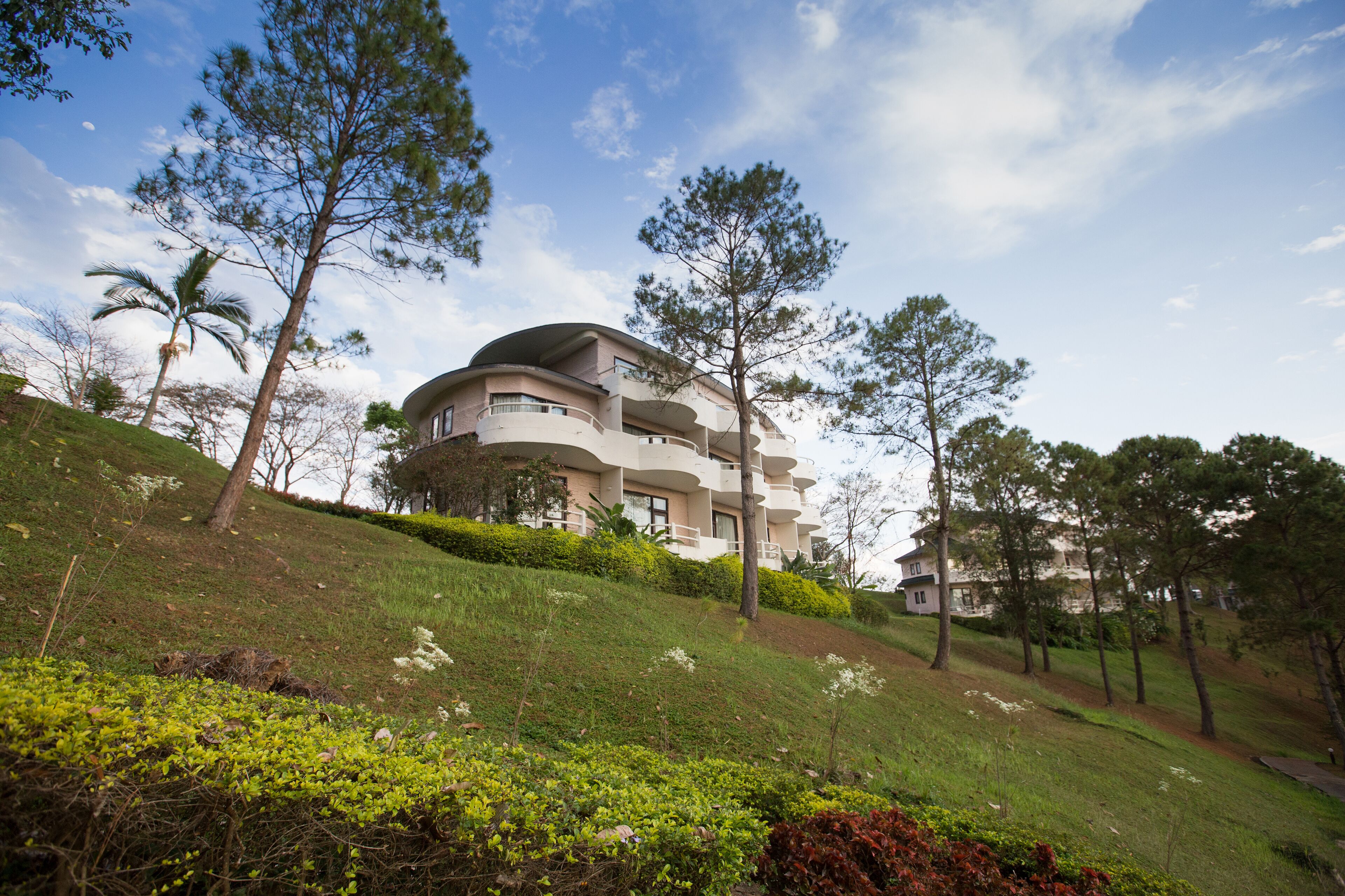 A multi-story building with balconies, surrounded by greenery and trees.