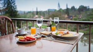 Ein Esstisch mit Speisen, Gläsern mit Wasser und Orangensaft, und Blick auf einen See und Bäume.