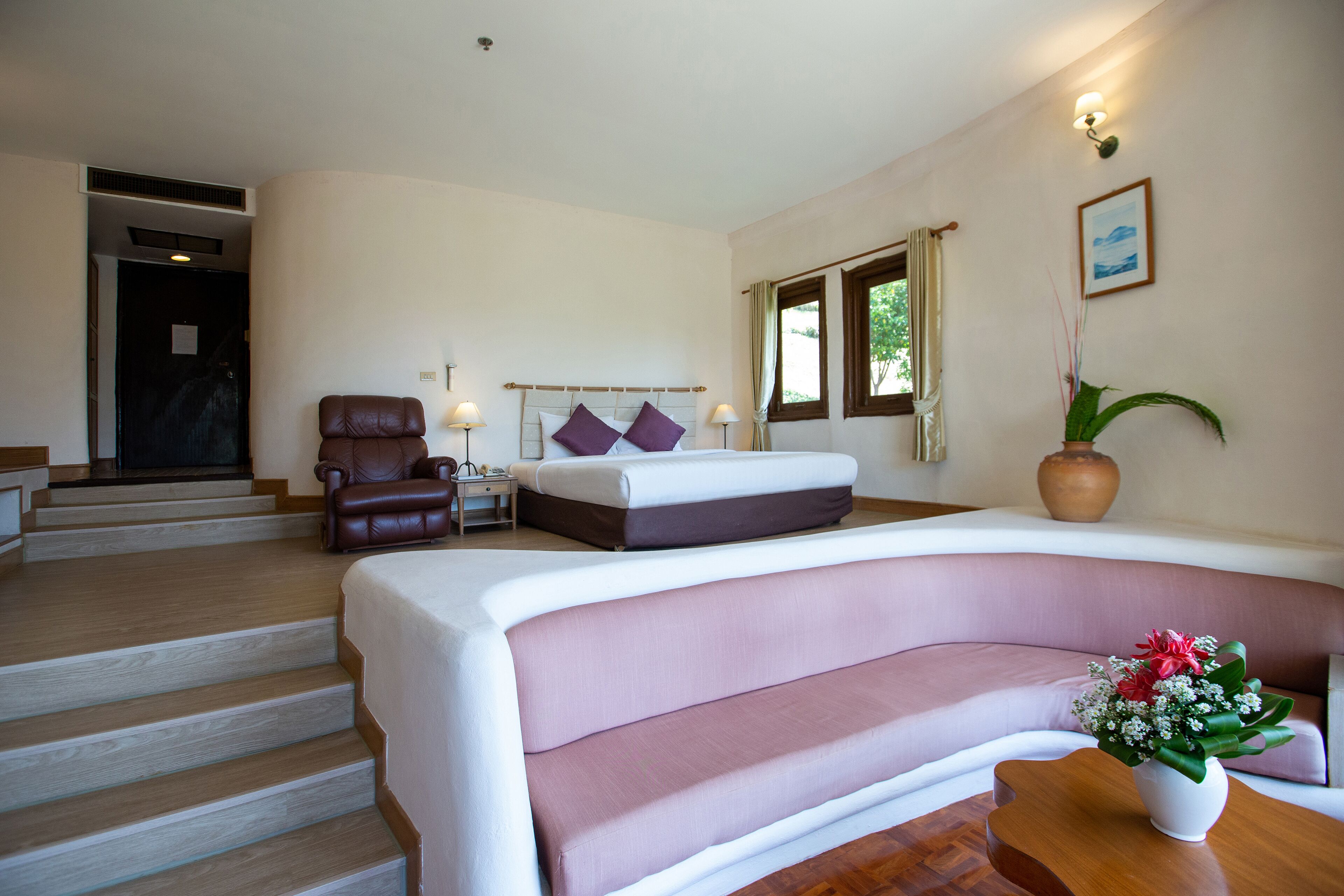 A bedroom with a bed, a sofa, a chair, a nightstand, and a potted plant.
