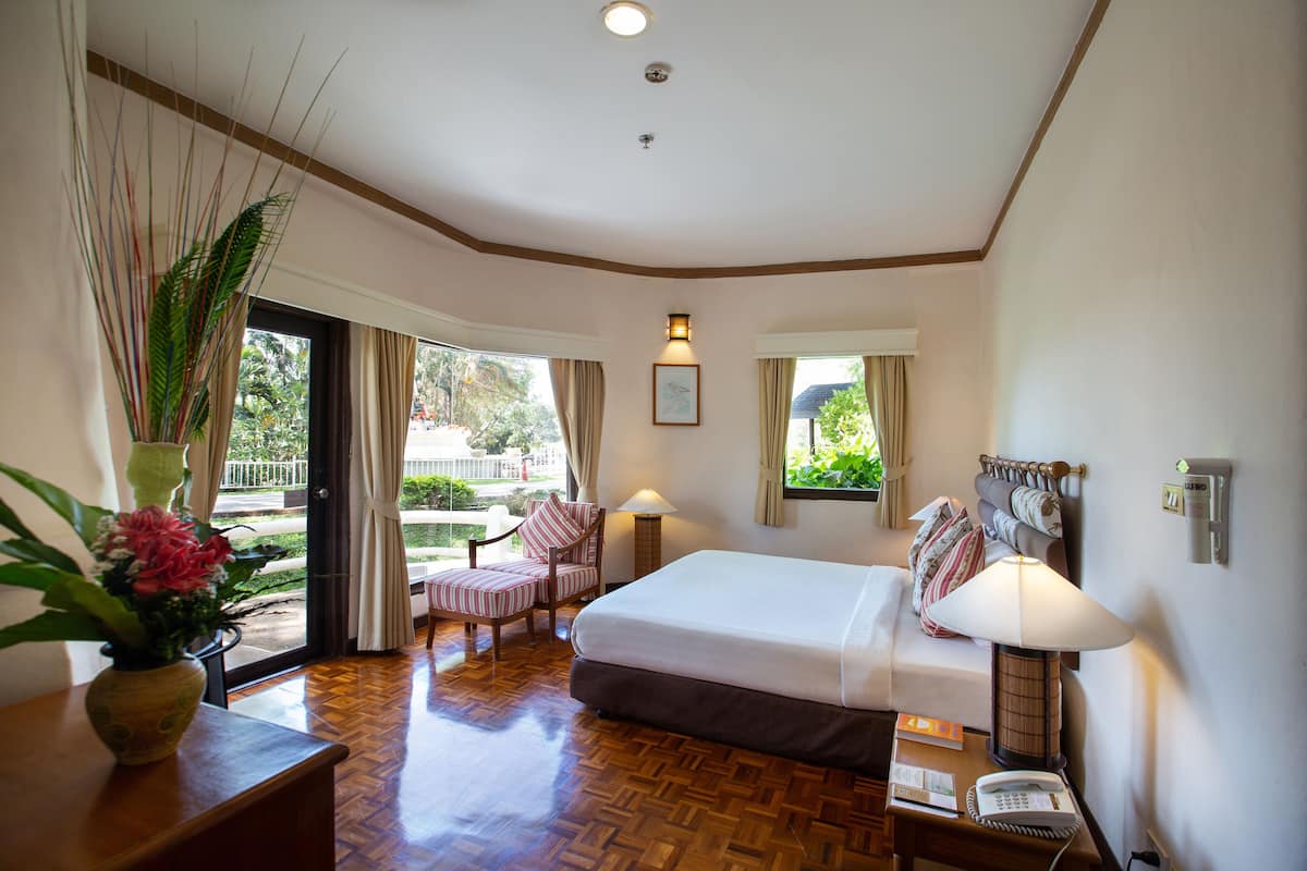 A hotel room with a bed, bedside table, lamp, phone, and a view of the outdoors.