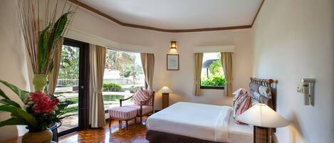 A hotel room with a bed, bedside table, lamp, phone, and a view of the outdoors.