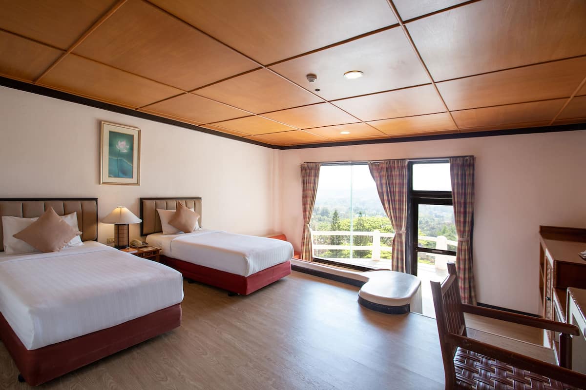 A hotel room with two beds, a desk, a chair, a window with curtains, and a painting on the wall.