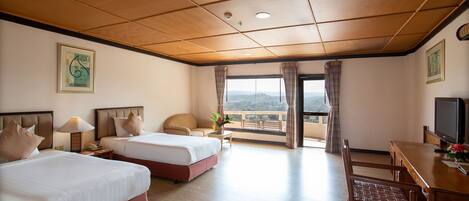 A hotel room with two beds, a desk with a TV, a chair, and a balcony with a view.