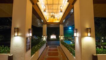A well-lit pathway leading to a building entrance with a signboard, surrounded by greenery.