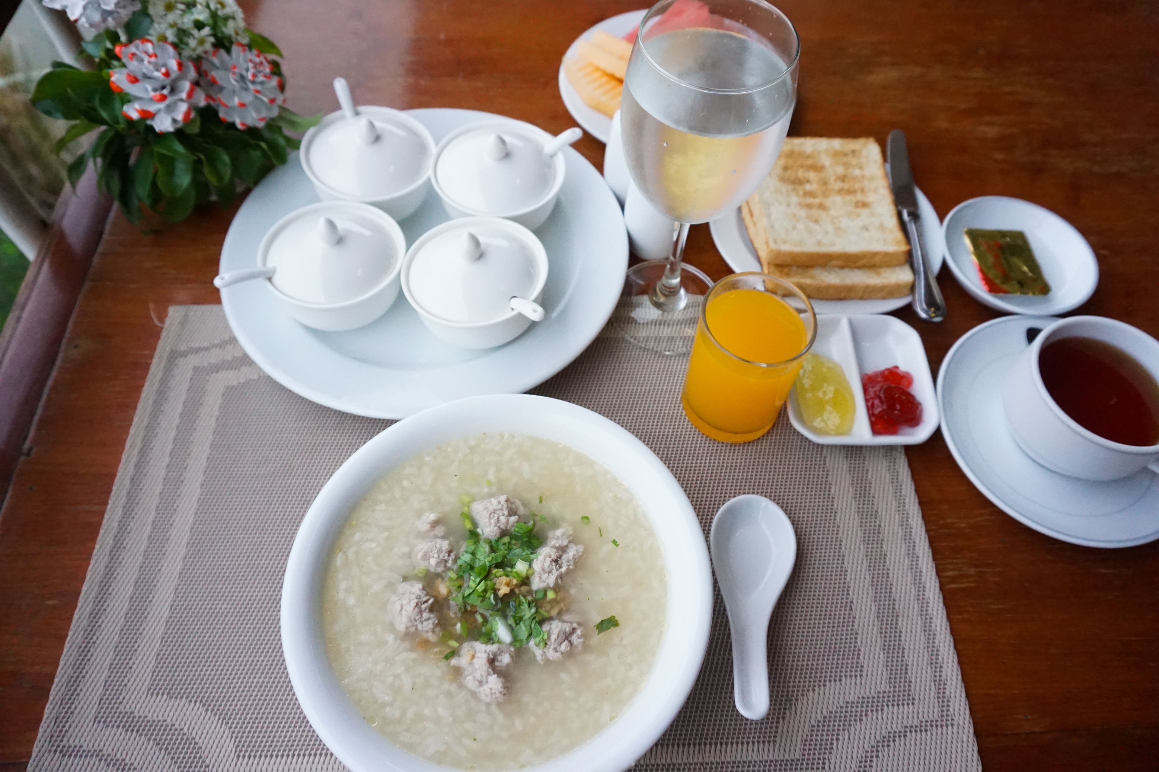 A breakfast setting with a bowl of soup, toast, orange juice, and tea.