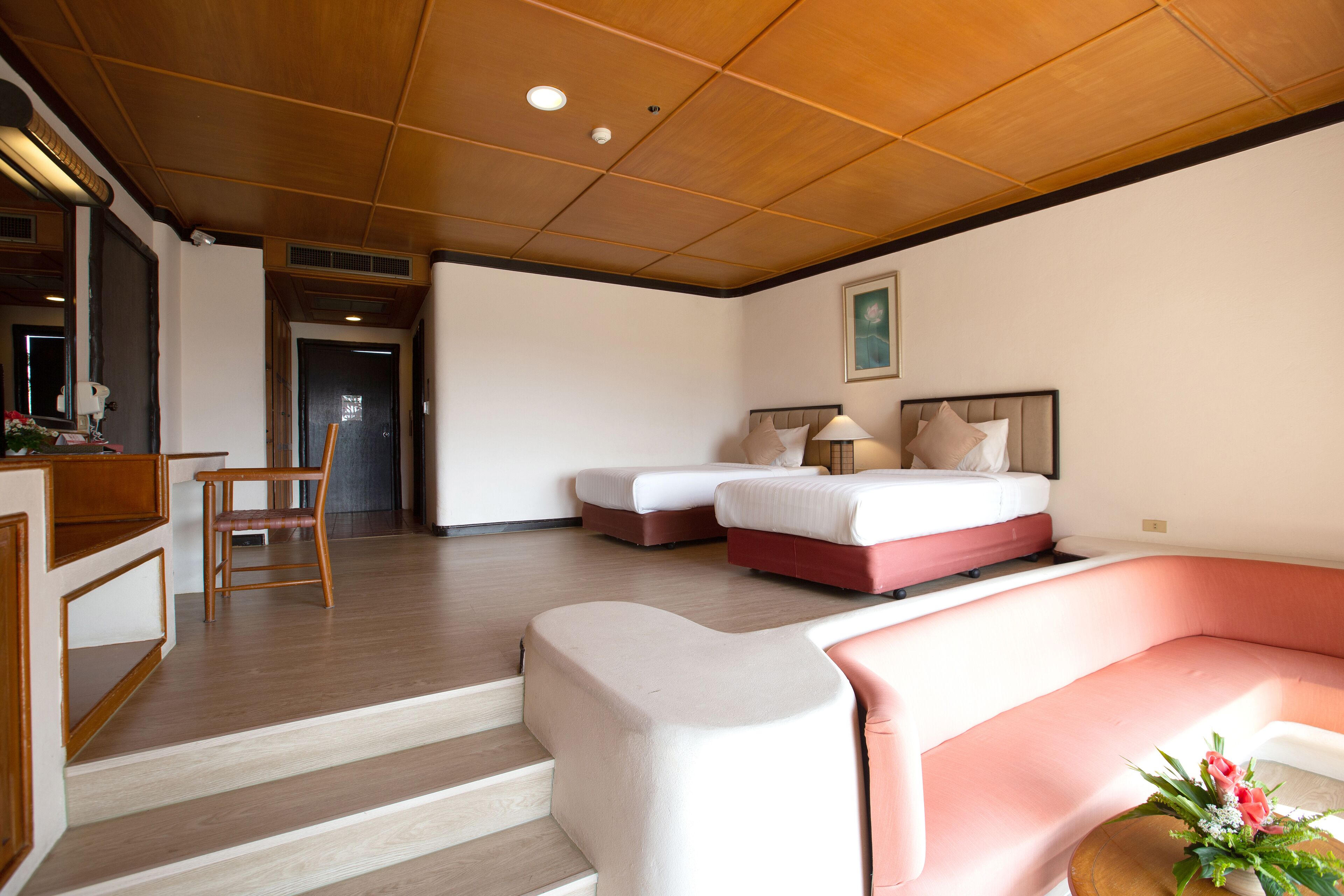 A hotel room with a wooden ceiling, a sofa, a bed, a desk, and a chair.