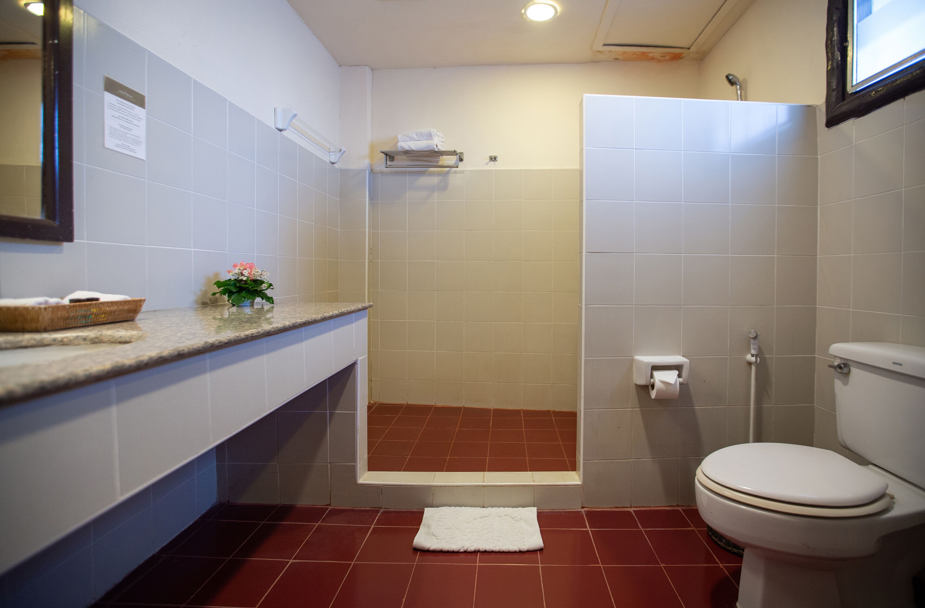 A bathroom with a white toilet, a shower, and a sink area with a towel rack and a basket.