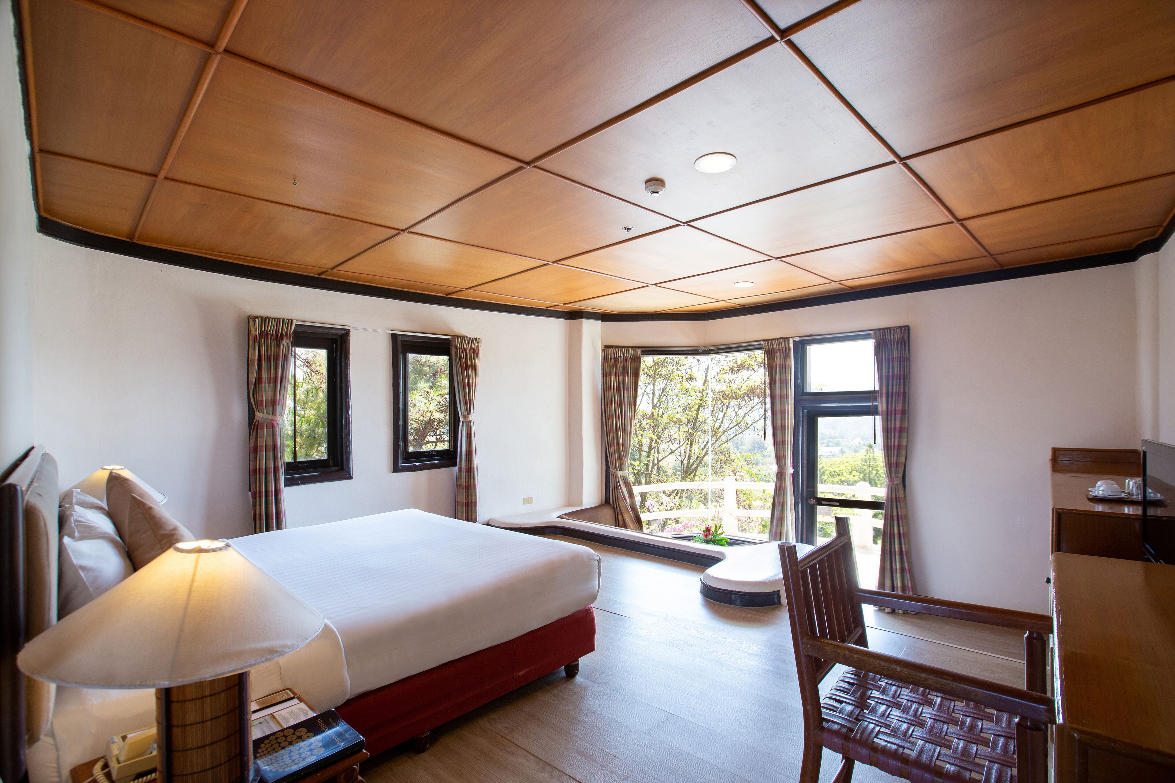 A hotel room with a bed, a desk, a chair, and a window with a view of greenery.
